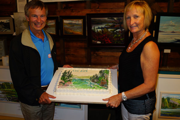 A man on the left and woman on the right hold a large decorated slab cake between them